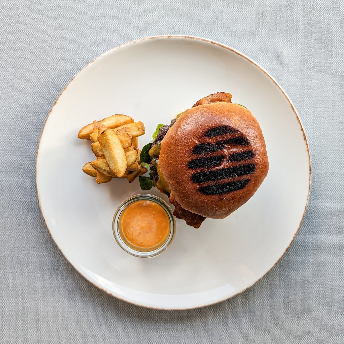 Cheeseburger med bacon, salat, tomat, relish, sød sennep, ketchup og mayonnaise og grove fritter