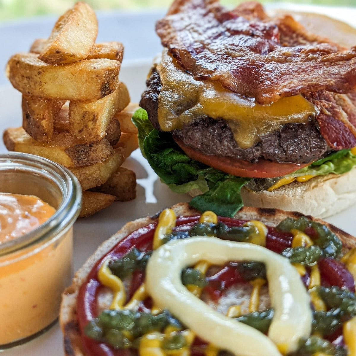 Cheeseburger med bacon, salat, tomat, relish, sød sennep, ketchup og mayonnaise og grove fritter